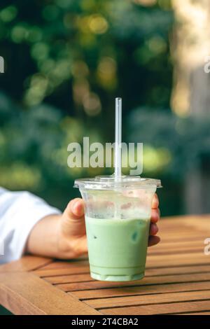 Latte matcha freddo in una tazza di plastica nelle mani di una donna. Foto Stock