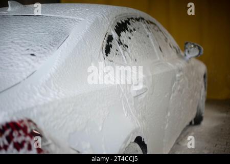 Macchina con sapone. Autolavaggio in città. Pulizia dell'auto dalla sporcizia. Schiuma bianca durante il trasporto. Foto Stock