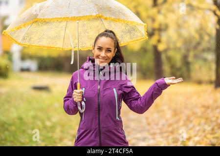 Ritratto di una giovane donna sorridente sotto un ombrello durante una passeggiata nel parco autunnale. Foto Stock