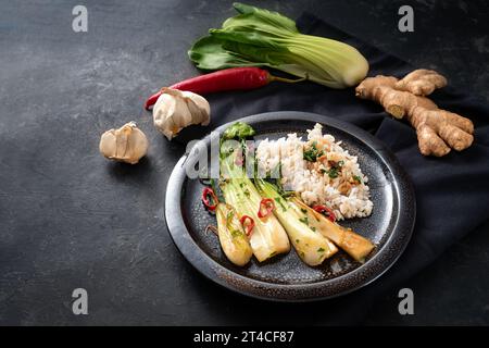 Pasto vegetariano da pak choi o cavolo cinese, fritto con aglio, zenzero, peperoncino rosso ed erbe, servito con riso su un piatto nero circondato Foto Stock