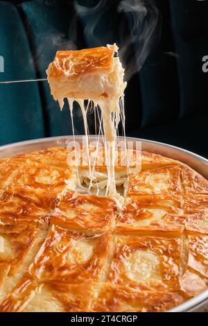 Pezzi di dolci orientali con pistacchi in un piatto bianco su un terreno bianco circondato da utensili in argento e rame Foto Stock