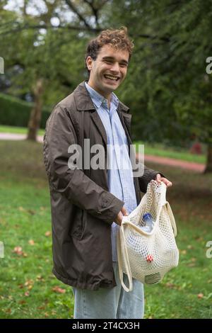 Giovane ragazzo urbano sorridente con il sacchetto di plastica per il riciclaggio nel parco, foto verticale Foto Stock