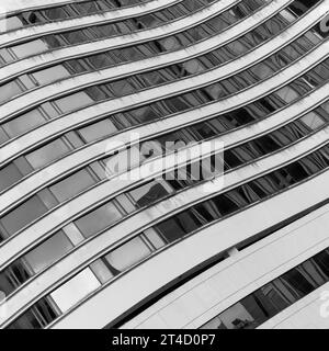 Questa immagine in scala di grigi cattura le forme sinuose di un edificio architettonico moderno. Le linee ondulate e fluide della facciata accentuano il senso del mo Foto Stock
