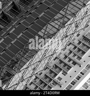 Questa immagine in scala di grigi mostra la giustapposizione di stili e strutture architettoniche. Il lato sinistro presenta una facciata moderna ed elegante caratterizzata da un'architettura b Foto Stock