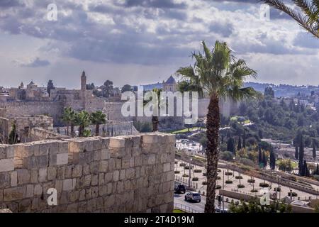 La strada, le palme e il giardino intorno alle mura della fortezza della città vecchia di Gerusalemme con la vista panoramica della città in Israele. Foto Stock