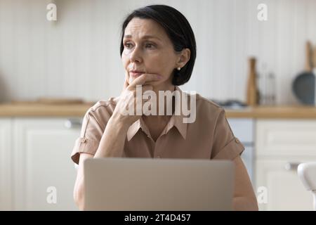Una donna ripugnante nel profondo del pensiero siede a un tavolo con un notebook Foto Stock