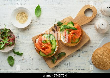 Sandwich di salmone affumicato aperti con formaggio cremoso, cetriolo, semi di sesamo, microgreen, spinaci, e foglie di piselli su sfondo di legno antico e chiaro. In salute Foto Stock