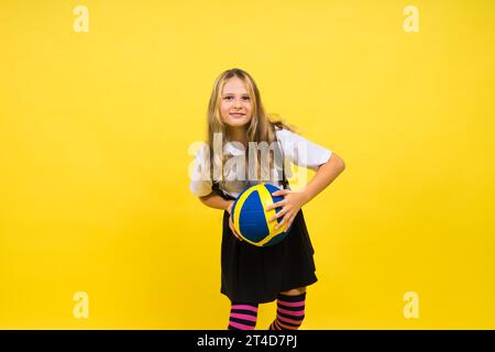 Una ragazza adolescente tiene in mano la palla da pallavolo e sorride su uno sfondo giallo rosso. Foto studio. Foto Stock