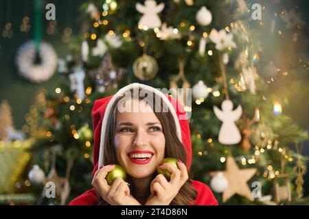 Natale. Elegante donna sorridente di 40 anni con ballo di Natale vicino all'albero di Natale nel moderno soggiorno. Foto Stock