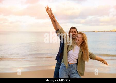 Giovane coppia romantica sulla spiaggia che si comporta come se stesse volando, con le braccia tese Foto Stock