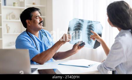 Medico indiano di mezza età che mostra radiografia toracica a pazienti di sesso femminile in clinica Foto Stock