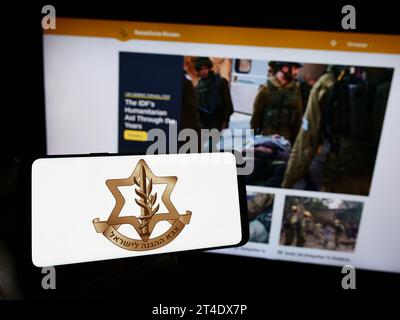 Persona in possesso di un cellulare con il logo delle forze militari israeliane (IDF) davanti alla pagina Web. Concentrarsi sul display del telefono. Foto Stock