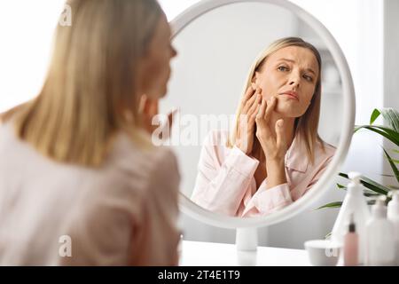 Problemi alla pelle. Sconvolta una donna di mezza età che guarda Pimples sulla sua guancia Foto Stock