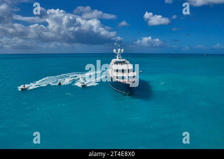 Foto aerea di un superyacht charter di lusso all'ancora in una baia isolata ad Antigua con moto d'acqua e tender che corrono. Foto Stock