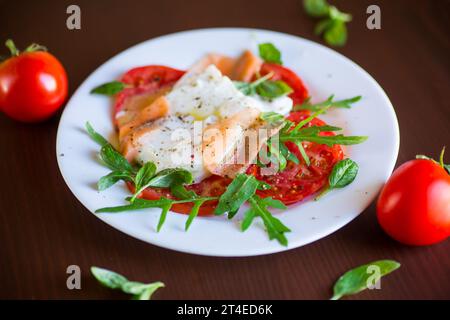 Uovo cotto in camicia con erbe, salmone leggermente salato e pomodori con spezie su un tavolo di legno. Foto Stock