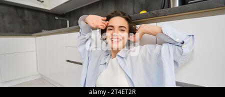 Ritratto ravvicinato di una bella donna sorridente, che tende le mani con il viso contento, si sente stanca, siede sul pavimento della cucina a casa sua Foto Stock