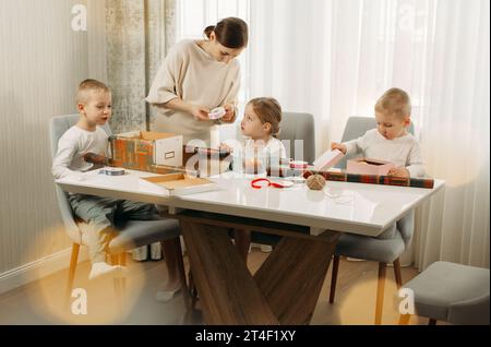 Una madre e i suoi figli si stanno preparando per Natale, facendo i regali. Famiglia in camera. Seduti al tavolo. Foto Stock
