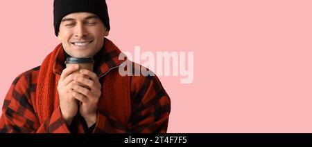 Giovane uomo felice in abiti invernali e con una tazza di caffè caldo su sfondo rosa Foto Stock