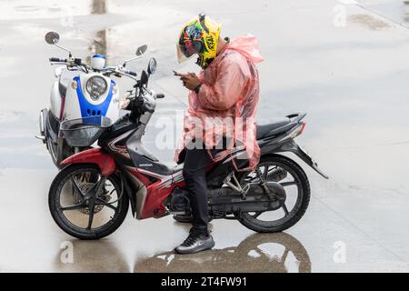 SAMUT PRAKAN, THAILANDIA, 20 settembre 2023, Un uomo con un impermeabile siede su una moto e guarda un telefono cellulare Foto Stock