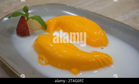 Budino di mango a forma di pesce con condimenti leciti, fragole e foglie di menta su un piatto bianco Foto Stock