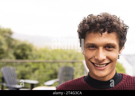 Ritratto dell'uomo birazziale felice con i capelli ricci sul balcone con vista sulla foresta, spazio fotocopie Foto Stock