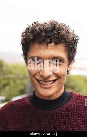 Ritratto dell'uomo birazziale felice con i capelli ricci sul balcone con vista sulla foresta Foto Stock