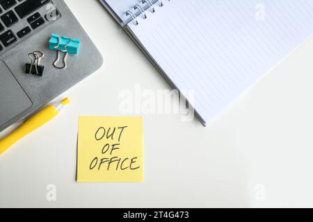 Vista dall'alto del notebook e del blocco note con il messaggio Out of Office scritto su un foglio adesivo giallo. Foto Stock