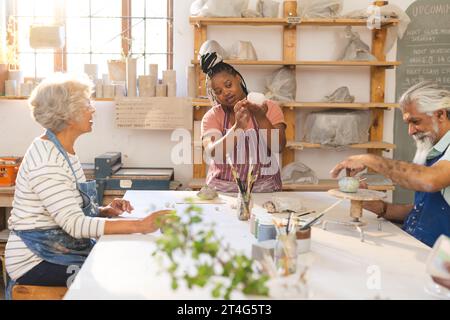 Allegri gruppo di ceramisti che hanno vetrato caraffe di argilla e che hanno discusso in uno studio di ceramica Foto Stock