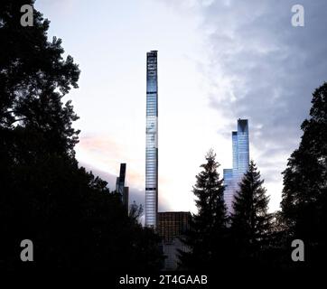 I grattacieli di New York City brillano contro le nuvole mentre cala la notte, visti attraverso gli alberi, con l'iconica Steinway Tower di lusso (111 W. 57) che sorge al centro. Foto Stock