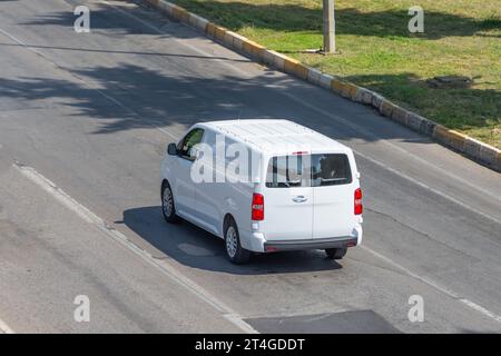 Bianco moderno furgone corriere cargo per piccole spedizioni che si muove velocemente lungo la strada autostradale fino alla periferia urbana della città. Business distribuzione e logistica Express S Foto Stock