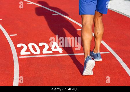 Runner attraversa la linea a partire dal 2024 su un tapis roulant rosso con i numeri 2024. Concetto di inizio anno nuovo, STEP Foto Stock