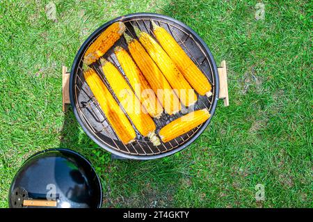 Barbecue rotondo con pannocchie di mais arrosto su prato verde Foto Stock