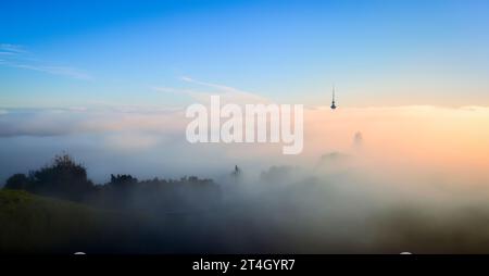 Auckland Sky Tower sopra un mare di nebbia. Vista dalla cima del monte Eden con il cratere vulcanico in primo piano. Auckland. Foto Stock