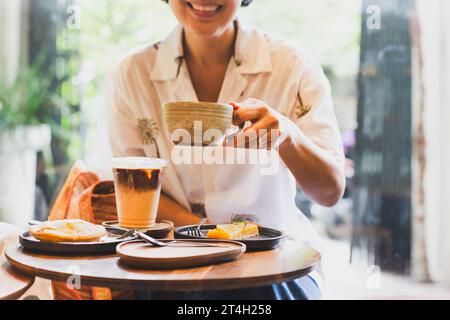 La donna felice beve caffè e mangia torta al bar. Foto Stock