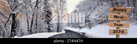 2024 felice anno nuovo scritto su un cartello direzionale in legno per una strada che attraversa una foresta innevata in montagna alpina Foto Stock