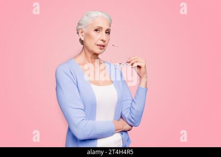 Bella bella vecchia signora dai capelli grigi che indossa casual, regge occhiali, pensa, rifletta. Isolato su sfondo viola pastello Foto Stock