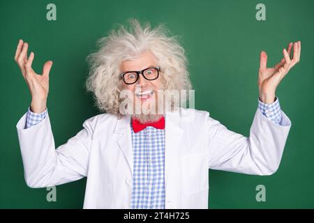 Foto di un pazzo e divertente scienziato medico con i capelli disordinati che ridono l'esperimento del male isolato su sfondo di colore verde Foto Stock