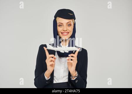 jolly arabian airlines hostess aerea in uniforme che mostra il modello dell'aereo e guarda la fotocamera in grigio Foto Stock