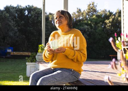 Donna birazziale anziana felice che beve tè seduto in giardino Foto Stock