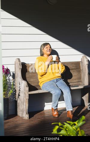 Donna birazziale anziana felice che beve tè seduto in giardino Foto Stock