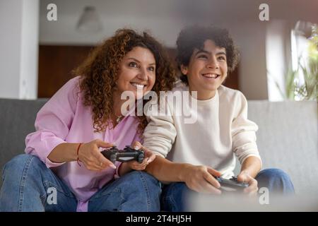 Madre e figlio che giocano ai videogiochi mentre sono seduti sul divano a casa Foto Stock
