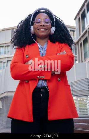 Verticale primo piano di una donna d'affari afroamericana sorridente che guarda la fotocamera con le braccia incrociate. Foto Stock