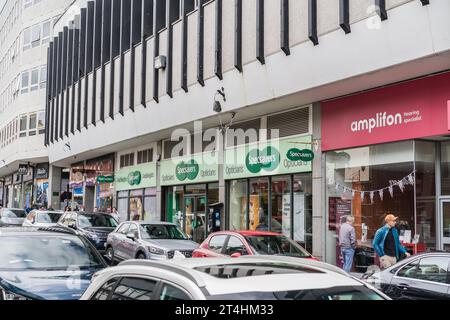 Shrewsbury, Shropshire, Inghilterra, 1 maggio 2023. Persone che passano davanti agli audioologi Amplifon e agli ottici Specsavers in strada con auto parcheggiate. Foto Stock