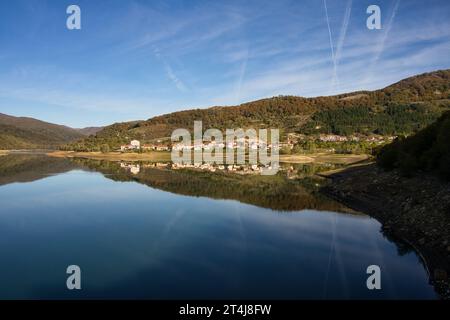 Idilliaco paesaggio naturale con un bellissimo lago e un villaggio che si riflette nelle acque pulite e calme in una giornata di sole. Ideale per progetti relativi a rur Foto Stock