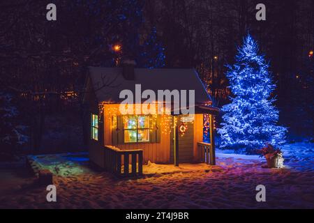 Casa da gioco privata per bambini in legno dipinto di giallo nel giardino domestico, decorata con luci a LED di Natale all'aperto in una notte fredda. Foto Stock