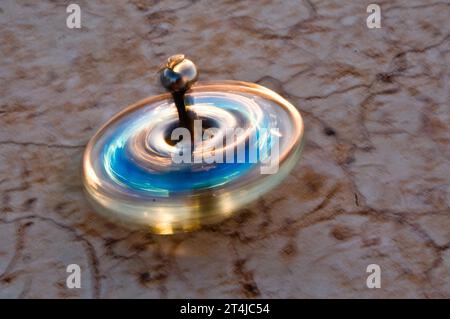 Piccolo dreidel Hanukkah in vetro blu e oro che gira in movimento su un muro di pietra. Foto Stock