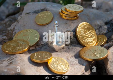 Un piccolo dreidel di Hanukkah argentato circondato da monete di cioccolato ricoperte in lamina d'oro. Foto Stock