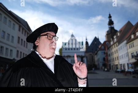 Lutherstadt Eisleben, Germania. 31 ottobre 2023. Dirk Wellmitz, guida della città nel ruolo di Martin Lutero, parla ai turisti sulla piazza del mercato. Per il giorno della riforma, i visitatori sono stati guidati attraverso il luogo di nascita del riformatore. Credito: Sebastian Willnow/dpa/Alamy Live News Foto Stock