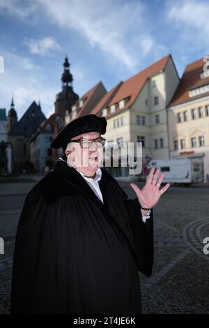 Lutherstadt Eisleben, Germania. 31 ottobre 2023. Dirk Wellmitz, guida della città nel ruolo di Martin Lutero, parla ai turisti sulla piazza del mercato. Per il giorno della riforma, i visitatori sono stati guidati attraverso il luogo di nascita del riformatore. Credito: Sebastian Willnow/dpa/Alamy Live News Foto Stock