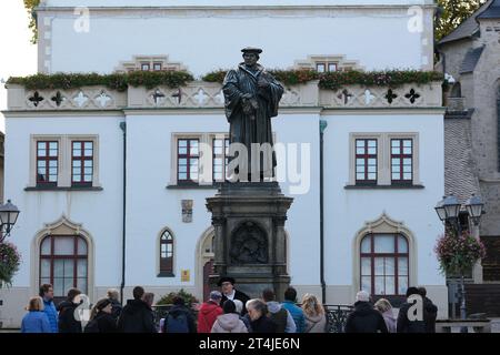 Lutherstadt Eisleben, Germania. 31 ottobre 2023. Dirk Wellmitz (M), guida della città nel ruolo di Martin Lutero, parla ai turisti di fronte al monumento di Lutero sulla piazza del mercato. Il giorno della riforma, i visitatori sono stati guidati attraverso la città dove è nato il riformatore. Credito: Sebastian Willnow/dpa/Alamy Live News Foto Stock